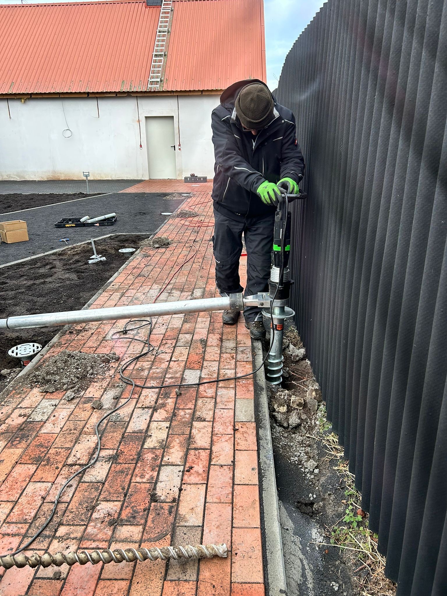 Setzen einer weiteren Schraube zwischen gepflasterter Fläche und Wand.